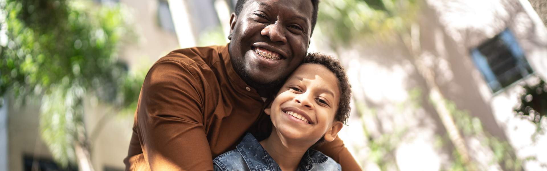 Main image: a father and son hugging and smiling outside in the sun.