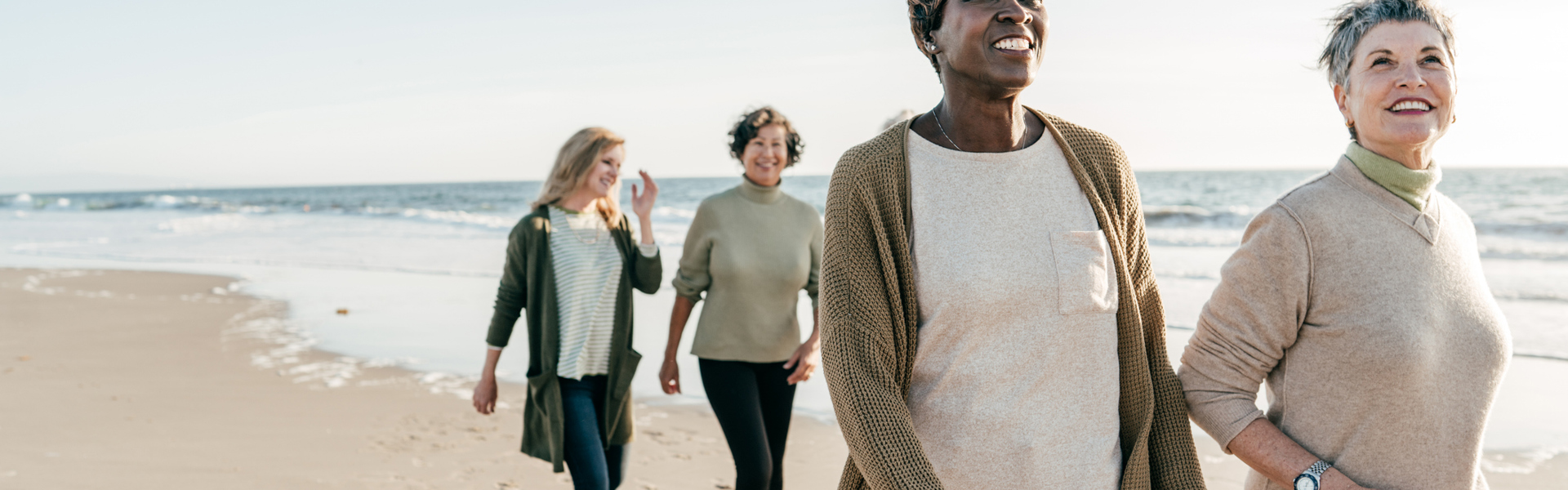 Main image: group of middle aged women walking on the beach, talking and smiling.